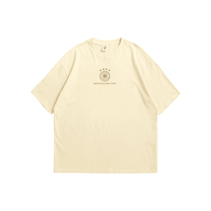 A cream oversized t-shirt shown from the front and back, featuring a small brown Germany DFB crest on the chest and a large intricate circular line-art illustration of German landmarks and four stars on the reverse - sports streetwear apparel by Stick-On Limited